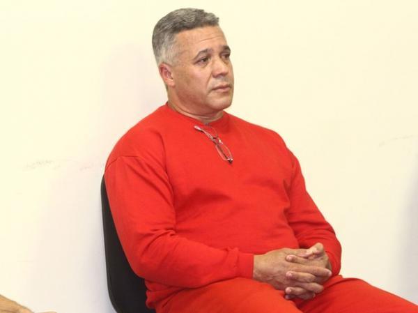 Bola está vestido com o uniforme vermelho da Subsecretaraia de Administração Prisional (Suapi). Na gola do moleton, ele carrega óculos de grau. (Imagem:Reprodução)
