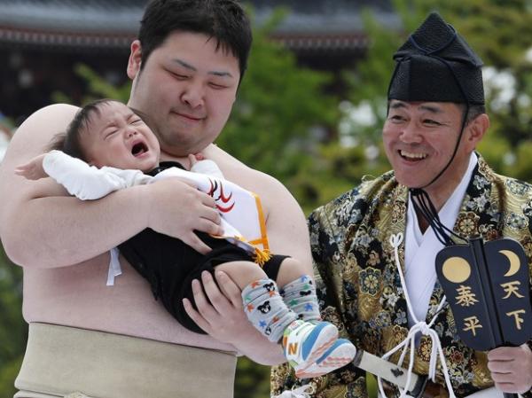 Jurado observa lutador de sumô segurando criança durante concurso de choro de bebê(Imagem:Reprodução)