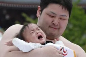 Jurado observa lutador de sumô segurando criança durante concurso de choro de bebê